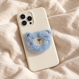 Support de téléphone en peluche ours bleu sur une coque crème — Cocooning
